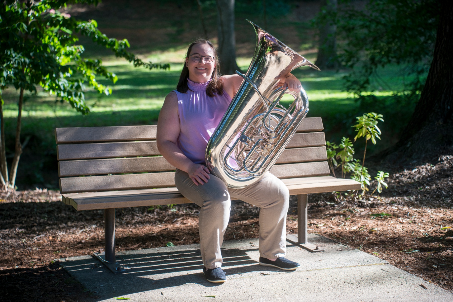 Music therapist smiling on a park bench holding a silver tuba