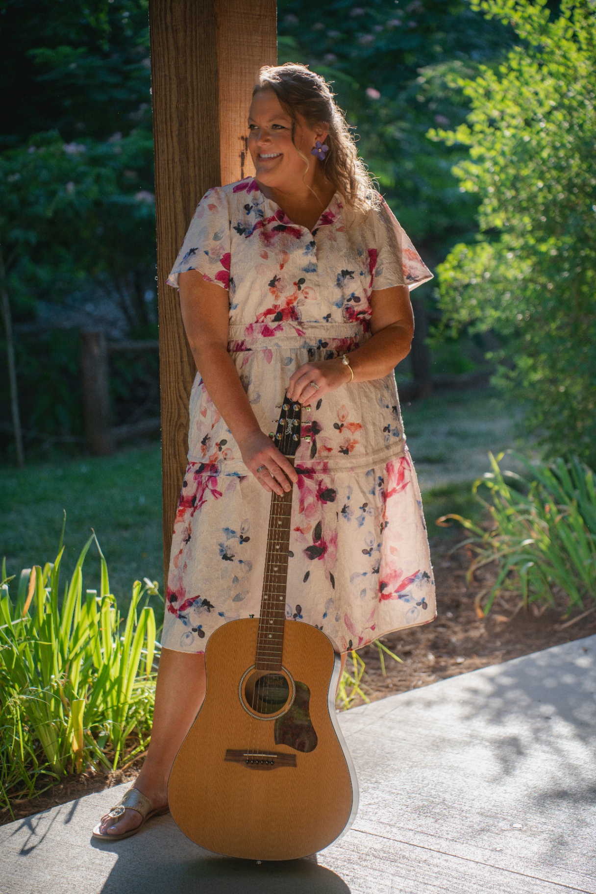 Music therapist in a floral dress leaning against a post with an acoustic guitar
