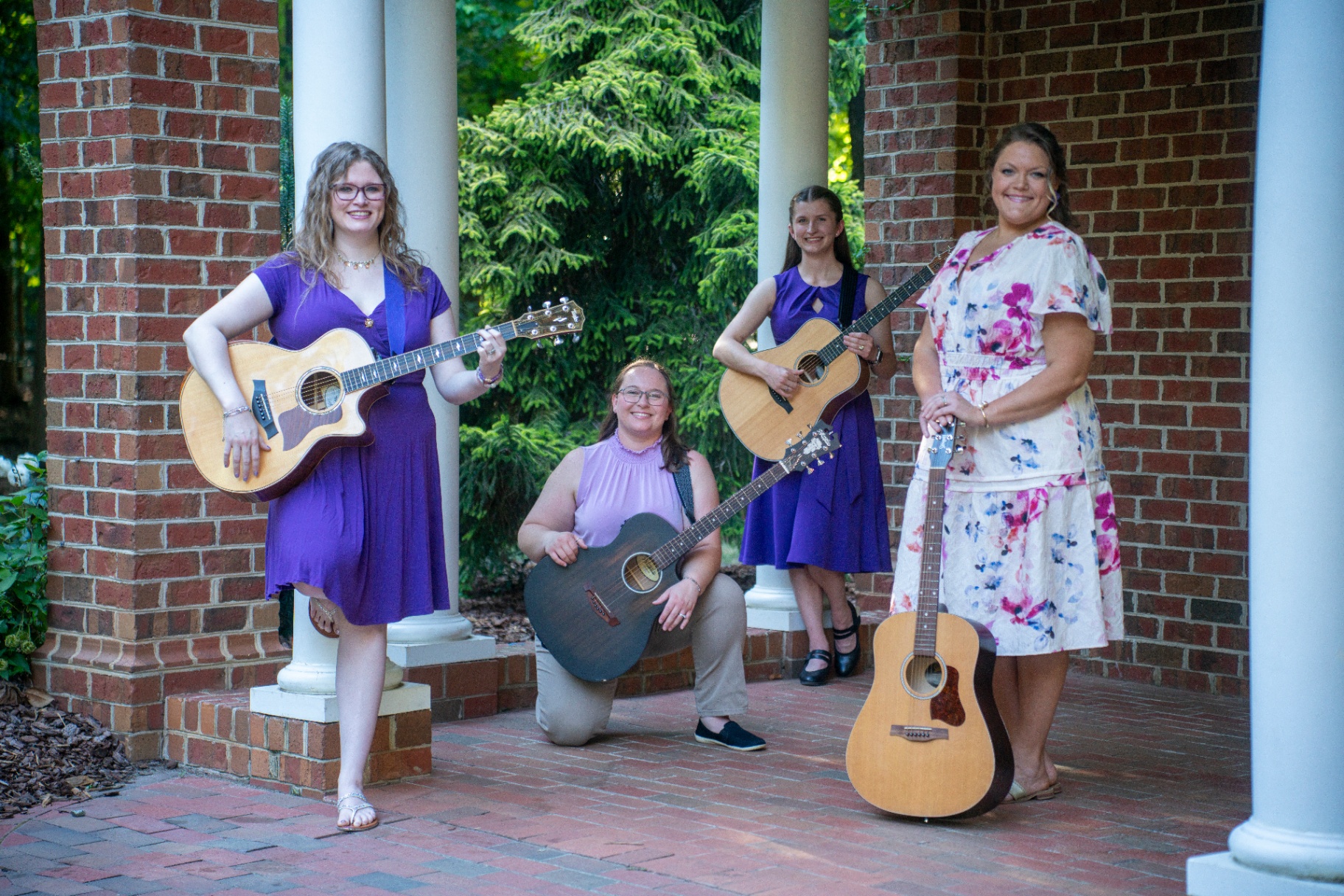 The Magnolia Melodies team of four therapists posing with acoustic guitars under a brick archway