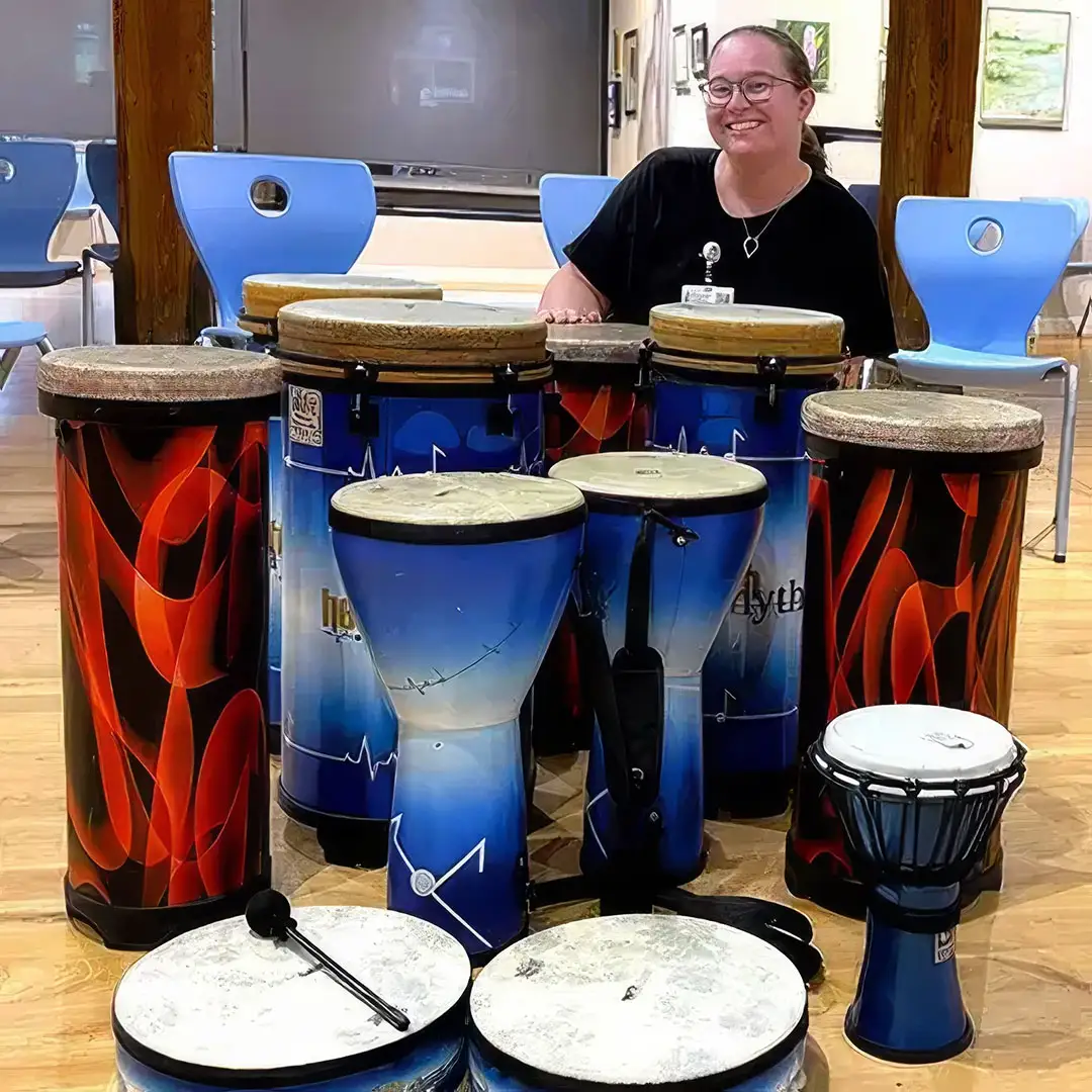 Mary smiling behind a colorful collection of hand drums