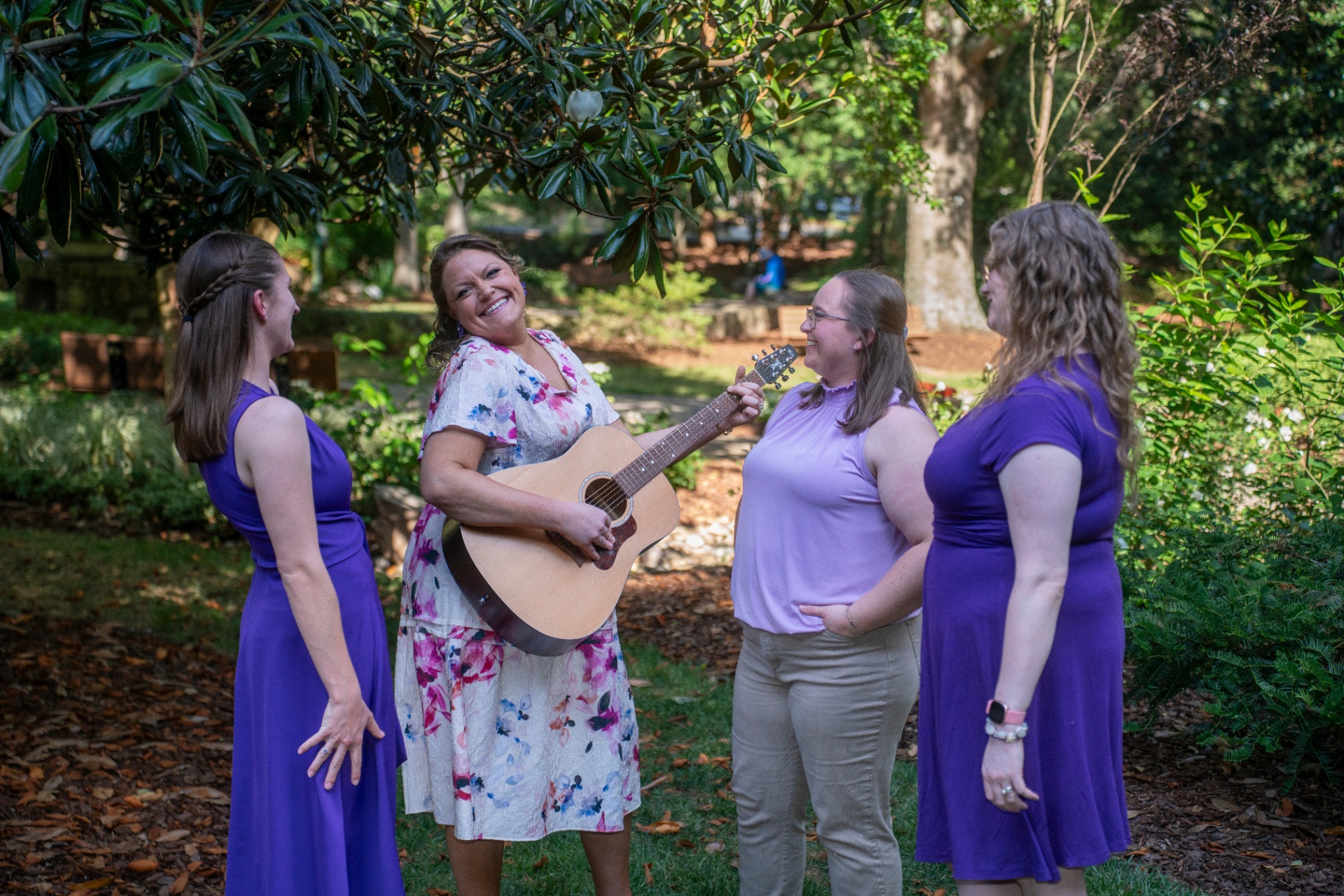 Magnolia Melodies music therapists smiling together in a garden, one holding an acoustic guitar