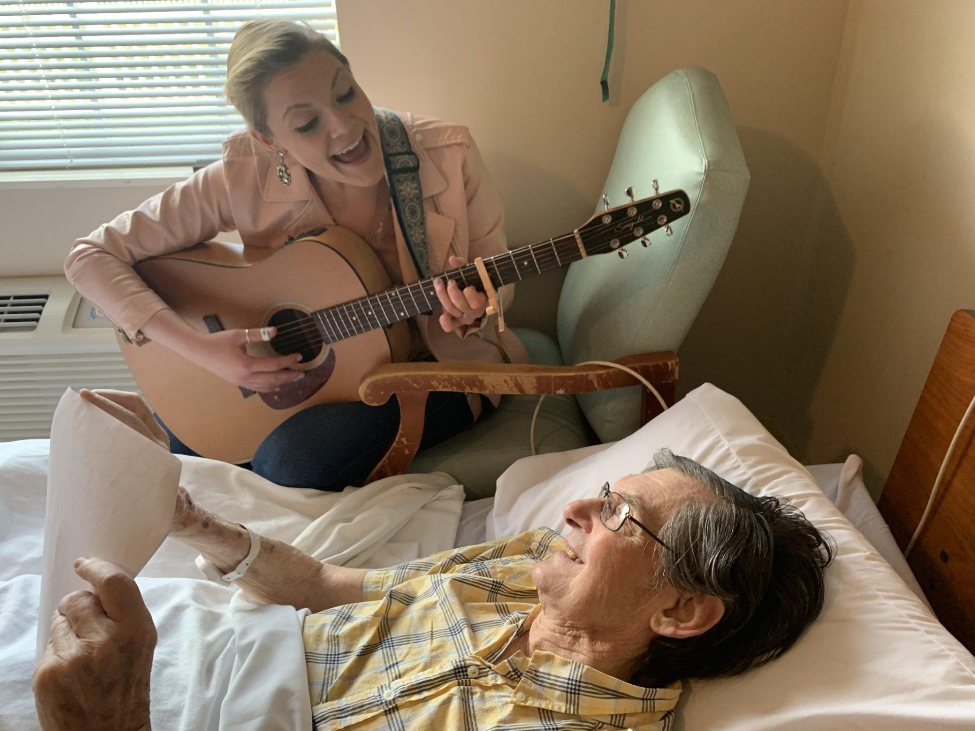 Music therapist playing guitar bedside for an older adult